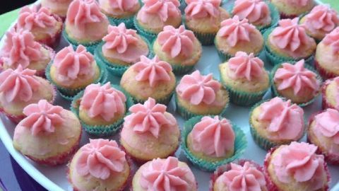 Bunte Cupcakes stehen auf einem weißen Teller, dekoriert mit rosa, veganem Frosting, umgeben von einem bunte Tischdecke.