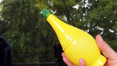 Einfach blitzblanke Fenster - hierfür Zitrone halbieren und die verschmutzen Fenster damit einreiben und danach ganz normal mit Spiritus reinigen. Eine Hand hält eine gelbe Zitronenflasche, während sie ein Fenster putzt, um es blitzblank zu machen.