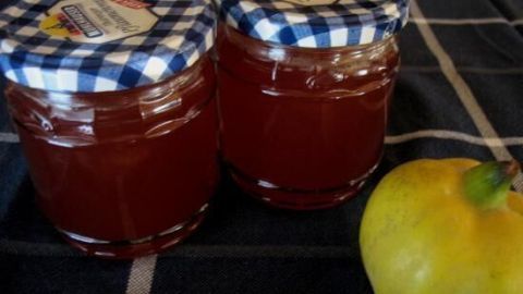 Zwei Glasbehälter mit Apfel-Quittengelee stehen auf einem karierten Tuch, neben einer frischen Quitte.