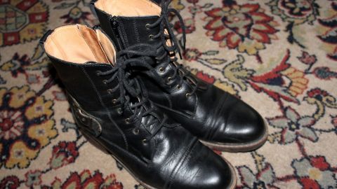 Schwarze Schuhe stehen auf einem gemusterten Teppich, bereit für das Dehnen, um besser zu passen und bequemer zu sein.