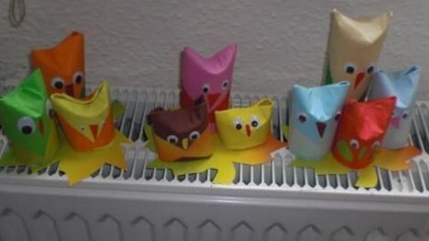 Bunte Eulen aus Klopapierrollen sitzen auf einem Heizkörper und zeigen fröhliche Gesichter in einer gemütlichen Umgebung.