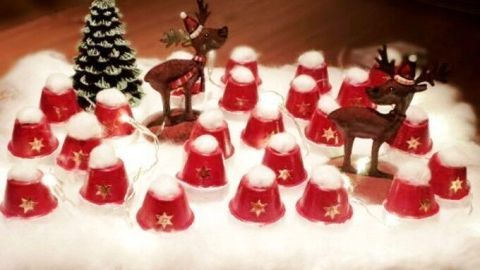 Rote Mini-Blumentöpchen stehen in einer festlichen Anordnung, umgeben von Weihnachtsdekor und Lichtern.