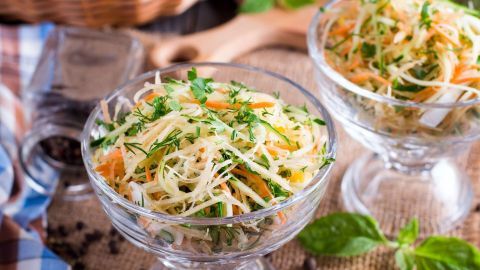 Zwei Glasdessertschalen zeigen bunten, frisch zubereiteten Möhren-Sellerie-Salat mit Kräutern, serviert auf einem rustikalen Tisch.