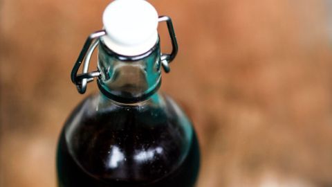 Die Haut von Babys ist sehr dünn und somit empfindlich, besonders am Popo. Erfahre hier, wie du den Babypopo mit Flaschenmilch und Olivenöl pflegen kannst. Ein Glasflasche mit verschlossenem Deckel steht auf einem Holztisch, neben ihr liegen einige Olivenzweige und Früchte.