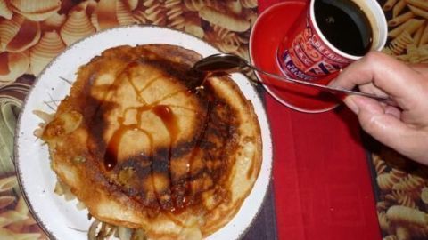 Ein gefüllter Pfannkuchen mit Apfel und Speck wird mit einer Gabel serviert, während eine Tasse Kaffee daneben steht.