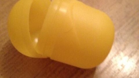 Ein gelber Plastikbehälter von Überraschungseiern liegt auf einem Holzfußboden, offen und bereit für eine Überraschung.