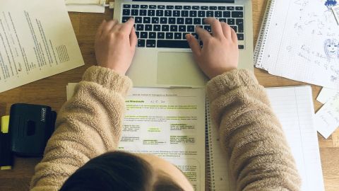 Mithilfe von selbstklebenden Türstoppern auf der Unterseite eines Notebooks, lassen sich Hitzestaus vermeiden. Ein Laptop wird genutzt, während Hände auf der Tastatur tippen. Der Tisch ist umgeben von Notizen und Unterlagen.