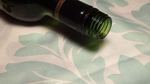 Rotwein auf weißer Tischdecke: Salz saugt Rotwein ganz einfach aus der Tischdecke heraus und der der Fleck ist schnell verschwunden. Eine halbleere Flasche Rotwein liegt schräg auf einer eleganten Tischdecke mit floralem Muster, die unversehrt aussieht.
