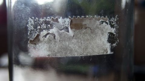 Mit Reinigungsbenzin Reste von Aufklebern entfernen. Ein Glas mit einer unansehnlichen, klebrigen Aufkleber-Reststelle zeigt, dass Reinigungsbenzin zur Entfernung gebraucht wird.