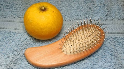 Eine Haarbürste liegt auf einem blauen Handtuch neben einer Zitrone, bereit zur Anwendung für glänzende Haare.