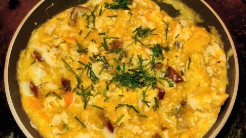 Eine goldene, cremige Rührei Deluxe mit frischen Kräutern wird in einer Pfanne serviert, umgeben von einer warmen Küchenszene.