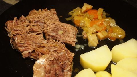 So werden Gulasch Rouladen und Rindfleisch superzart. Einfach nach dem Anbraten mit Mineralwasser ablöschen. Zartes Rindfleisch liegt auf einem Teller, umgeben von gedünstetem Gemüse und Kartoffeln, appetitlich angerichtet.