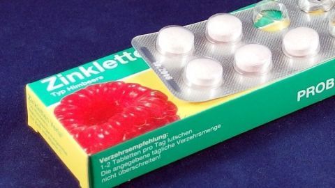 Ein Pillenblister mit mehreren Tabletten liegt auf einer bunten Verpackung. Der Kontext zeigt eine flache, einfarbige Oberfläche.