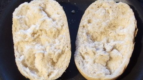 Aufbackbrötchen sind aufgeschnitten und zeigen eine trockene, bröselige Innenseite in einer Pfanne.