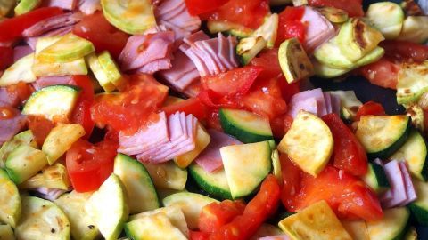 Bunte Gemüsestreifen und Schinkenstückchen werden in einer Pfanne gebraten, um gesunde Mahlzeiten beim Abnehmen zuzubereiten.