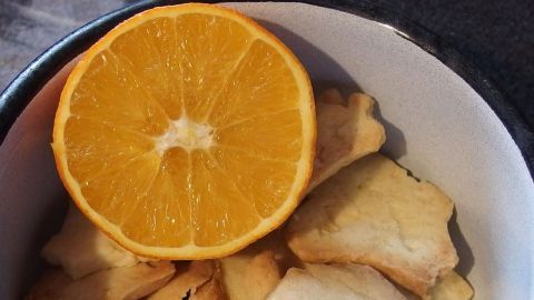 In einer Schüssel liegen trockene Plätzchen mit einer frisch aufgeschnittenen Orange, die zur Wiederherstellung der Weichheit dient.