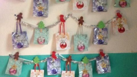 Adventskalender hängt an der Wand, bestehend aus bunten Tüten mit Nummern, festgemacht an glitzernden Girlanden.