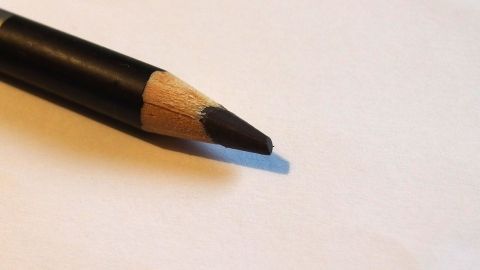 Ein schwarzer Kajalstift liegt auf einem weißen Blatt Papier und ist bereit, verwendet zu werden, ohne einen Abdruck im Augenlid zu hinterlassen.
