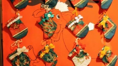 Bunte Adventssäckchen sind an einer roten Wand mit Rehgeweihen befestigt und strahlen festliche Stimmung aus.