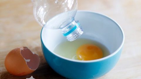 Eine Plastikflasche hebt Eigelb aus einer Schüssel, während Eiweiß darin gesammelt wird; neben einer aufgebrochenen Eierschale.