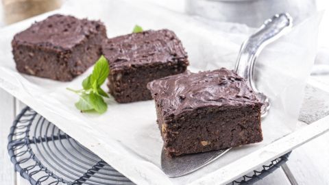 Drei schokoladige Mokka-Brownies liegen auf einem weißen Teller, umgeben von frischen Minzblättern auf einem dekorativen Gitter.