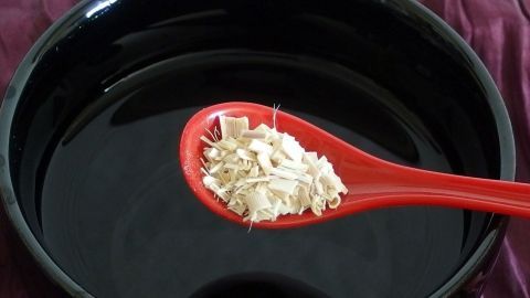Eine rote Kelle mit Ingwer liegt über einer schwarzen Schüssel mit Wasser, bereit für die Zubereitung von Ingwertee.