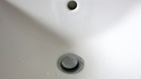 Ein weißes Waschbecken mit Wasserflecken, während Wasser langsam durch den Abfluss läuft, um Kalkflecken zu vertreiben.