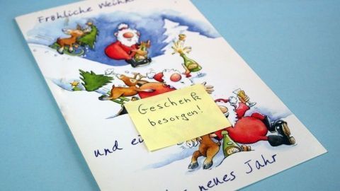 Ein buntes Weihnachtskartenmotiv zeigt Santa und fröhliche Tiere, während ein Zettel mit "Geschenk besorgen!" aufklebt.