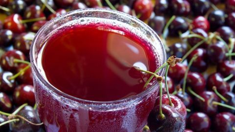 Ein Glas Kirschsaft steht im Vordergrund, umgeben von frischen Kirschen, was gesundes Trinken symbolisiert.
