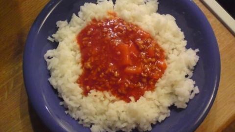 Ein blauer Teller gefüllt mit weißem Reis, der in der Mitte mit einer roten Tomatensauce bedeckt ist, auf einem Holztisch.