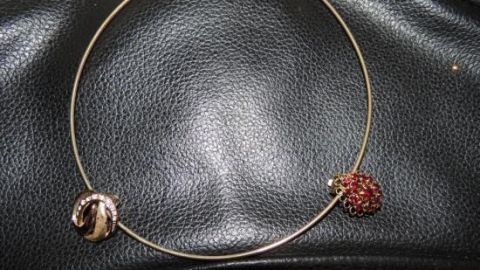 Ein minimalistisches Schmuckstück mit einem dünnen Goldhalsring und zwei Anhängern liegt auf einem schwarzen Lederuntergrund.