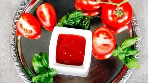 Ein glasierter Teller zeigt frische Tomaten und selbstgemachten Ketchup, umgeben von frischen Basilikumblättern.