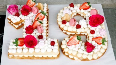 Zwei große Zahlen aus Kuchen, dekoriert mit Sahne und frischen Früchten, stehen auf einem weißen Brett im Freien.