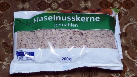 Eine Tüte mit gemahlenen Haselnusskernen liegt auf einem gemusterten Hintergrund, bereit zum Kochen oder Backen.
