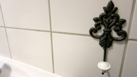 Verwende Autoshampoo, um deine Badezimmerfliesen zum Glänzen zu bringen. Ein einfacher und effektiver Trick, der hartnäckigen Schmutz entfernt und deine Fliesen wie neu erscheinen lässt. Probiere es im nächsten Putzgang aus! Ein verzierter Haken hängt an glänzenden Badezimmerfliesen neben einem weißen Waschbecken.