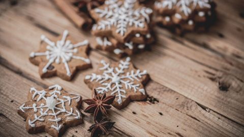 Leckere Duftsterne aus Lebkuchen liegen auf einer rustikalen Holzoberfläche, umgeben von Zimtstangen und Sternanis.