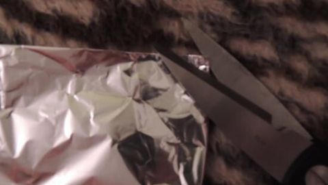 Eine Schere schneidet in Aluminiumfolie, um Kleidung draußen ohne Vogel- und Fliegendreck zu lüften.