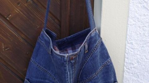 Eine Tasche aus alten Jeans hängt an einer Holzplatte, die eine kreative Weiterverwertung von Denim zeigt.