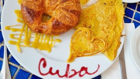 Ein Croissant und eine herzhafte Omelette auf einem Teller mit der Aufschrift „Cuba“ vor einem blauen Mosaiktisch.