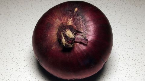 Aufgeschnittene Zwiebel gegen verstopfte Nase in der Nacht. Eine rote Zwiebel liegt auf einer hellen, strukturierten Oberfläche, bereit zur Verwendung gegen eine verstopfte Nase.