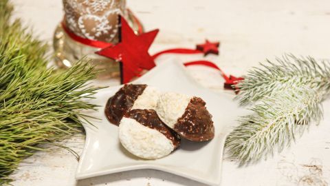 Kokosmakronen liegen auf einem Sternteller, umgeben von Weihnachtsdekoration wie einer Kerze und Tannenzweigen.