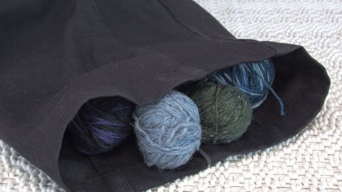 Ein schwarzer Zugluftstopper liegt mit bunten Wollknäueln gefüllt auf einem Teppich und schützt vor kaltem Luftzug.