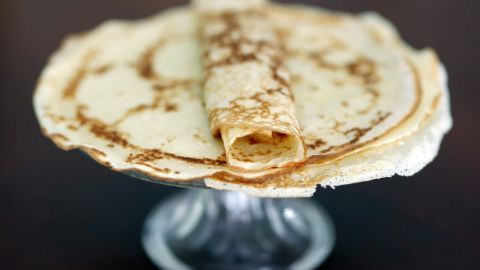 Auf einem Glasteller liegen Hefepfannkuchen, lose übereinander gestapelt und einer ist aufgerollt.