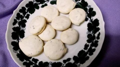 Ein Teller mit Anisplätzchen liegt auf einem lila Tuch. Die Plätzchen sind rund und hell, umgeben von dunklem Muster auf dem Teller.