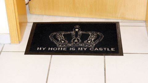 Ein schwarzer Fußmatte mit einer Krone, die den Spruch „MY HOUSE IS MY CASTLE“ zeigt, liegt vor einer Haustür im Flur.