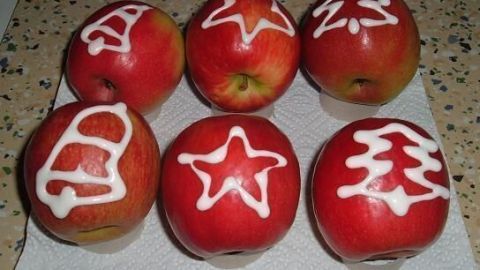 Rote Äpfel sind mit Zuckerguss geschmückt, der weihnachtliche Motive zeigt, auf einer Arbeitsfläche angeordnet.