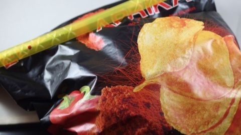 Eine Tüte Chips liegt auf einer Fläche, während ein Lineal daneben positioniert ist, um die Größe zu verdeutlichen.
