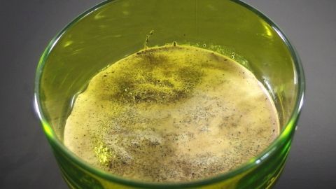 Ein grüner Glasschälchen enthält eine schaumige, dicke Mischung, die für ein Hautpeeling vorbereitet ist.