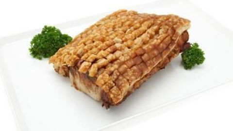 Ein Krustenbraten mit knuspriger Kruste liegt auf weißem Teller, umgeben von grüner Petersilie.