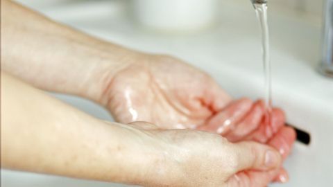 Hände halten sich unter einem Wasserhahn, während Wasser fließt; das Bild vermittelt hygienische Reinlichkeit.